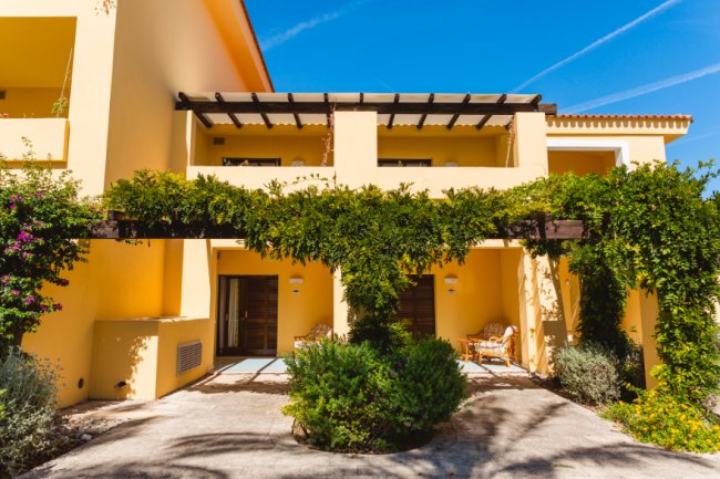 Edificio giallo con pergolato e vegetazione.