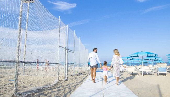 Famiglia passeggia sulla spiaggia sotto cieli blu.
