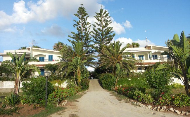 Ingresso alberato con due edifici bianchi ai lati.