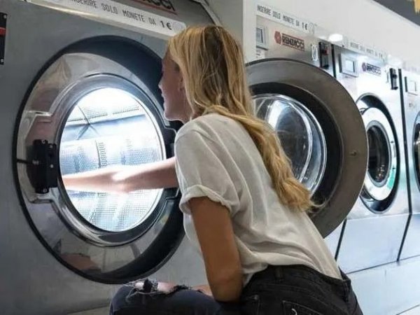 Donna di profilo inserisce biancheria in una lavatrice a oblò.