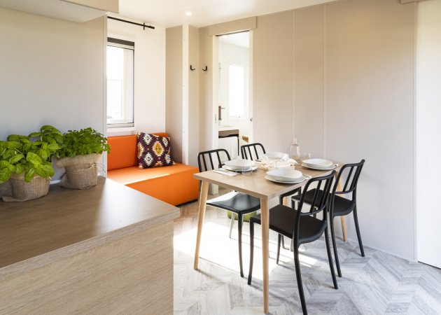 Sala da pranzo moderna con tavolo apparecchiato e sedute nere, divano arancione sullo sfondo.