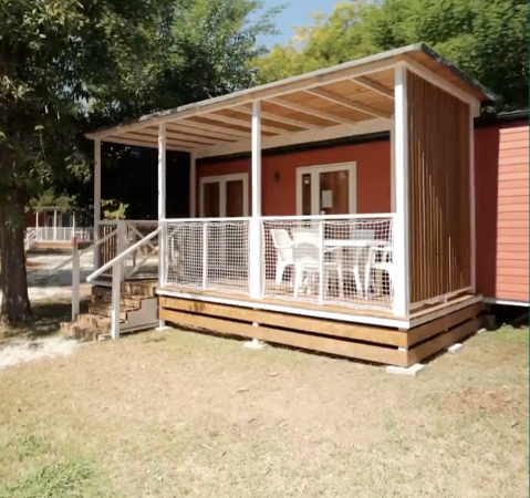 Un bungalow con veranda in legno e sedie bianche.