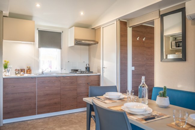 Cucina moderna con mobili in legno, tavolo apparecchiato, e una finestra con tende grigie.