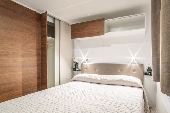 Letto matrimoniale in una camera moderna con testiera imbottita e armadio a muro.
