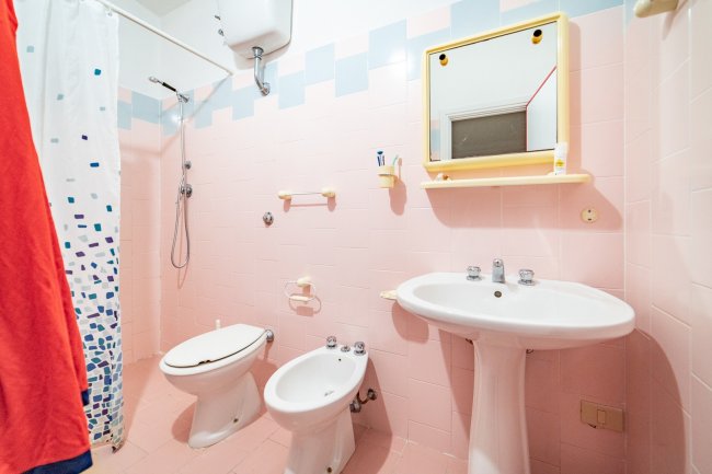 Bagno con piastrelle rosa, sanitari, lavandino e specchio giallo.