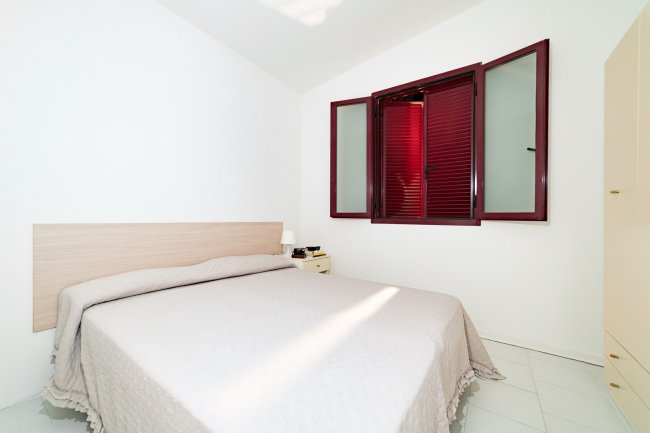 Camera da letto con letto matrimoniale, finestra con persiane rosse.