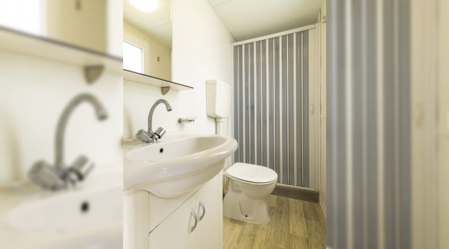 Bagno compatto con doccia, lavabo bianco e WC. Dettaglio su superfici chiare.