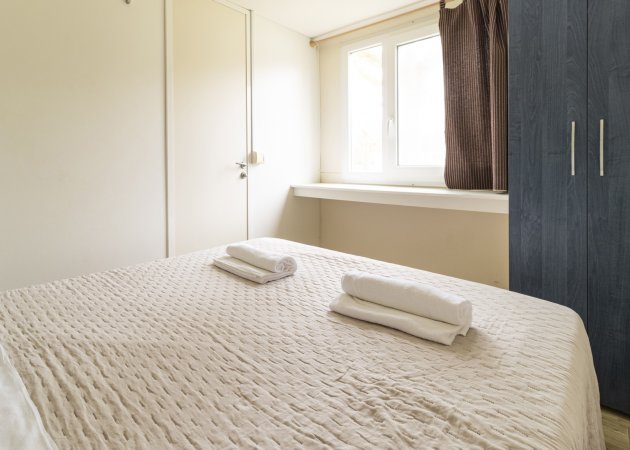 Camera da letto con letto matrimoniale, due asciugamani piegati, armadio blu e finestra.