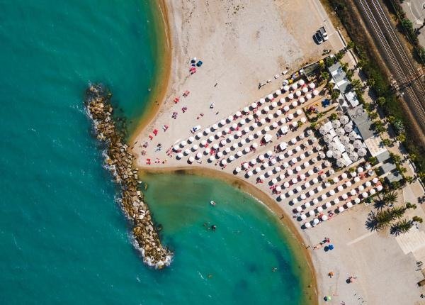 Spiaggia con ombrelloni disposti ordinatamente, una barriera di pietre e mare azzurro.
