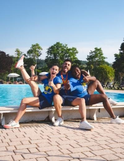 Tre persone sorridenti in abbigliamento sportivo blu sedute sul bordo di una piscina.