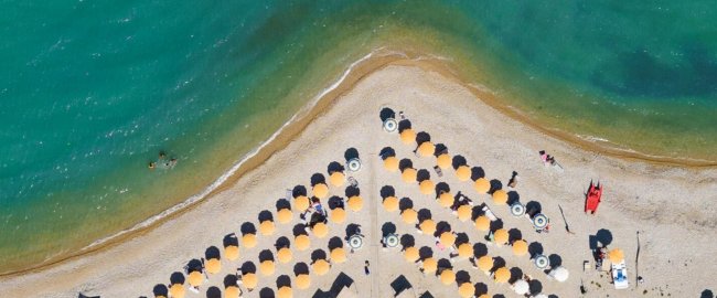 Ombrelloni gialli disposti a fila su una spiaggia, vicino a un mare turchese.