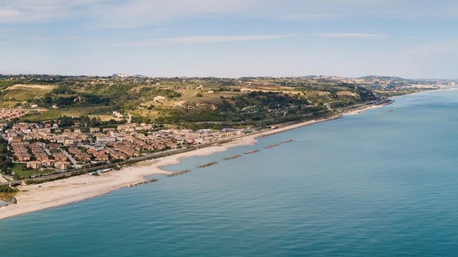 Vista aerea di una costa con case, vegetazione e mare sereno.