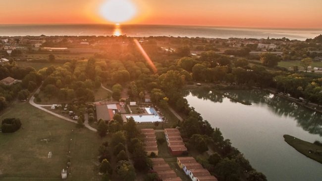 Tramonto su un paesaggio con lago, case e alberi, riflesso sull'acqua.