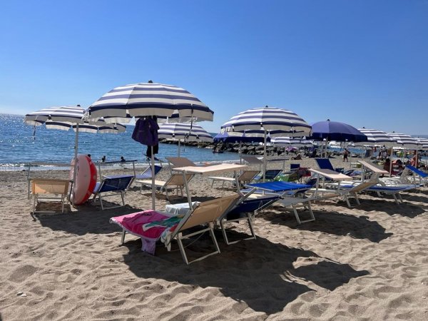 Spiaggia con ombrelloni e lettini blu a righe bianche.