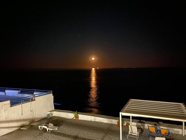 Luna piena sopra il mare con riflessi dorati sull'acqua.