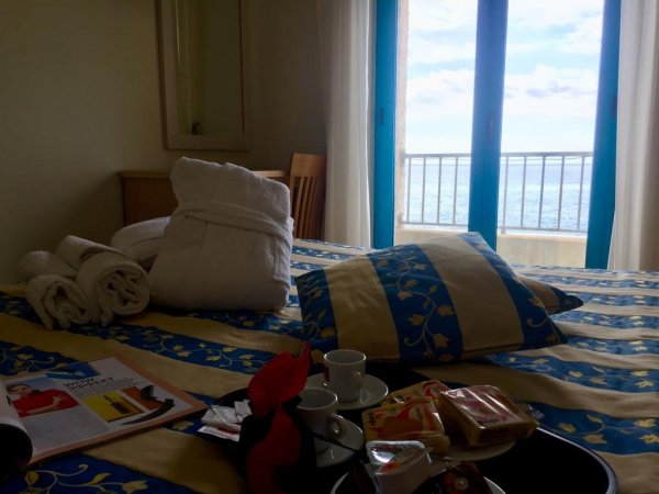 Stanza con letto colorato, finestra vista mare e vassoi per caffè.