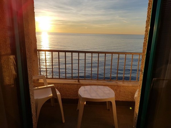 Balcone con sedie bianche che si affaccia su un tramonto sul mare.