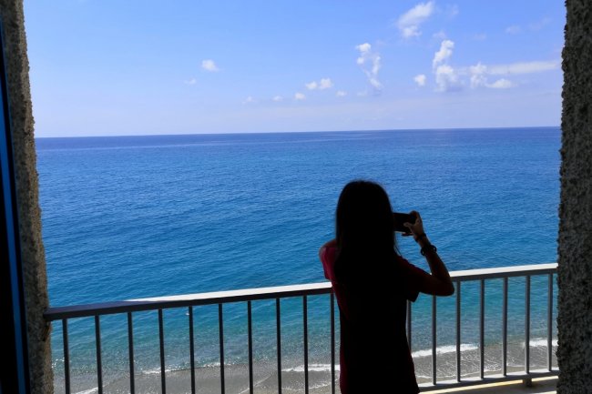 Persona fotografa l'oceano dal balcone.