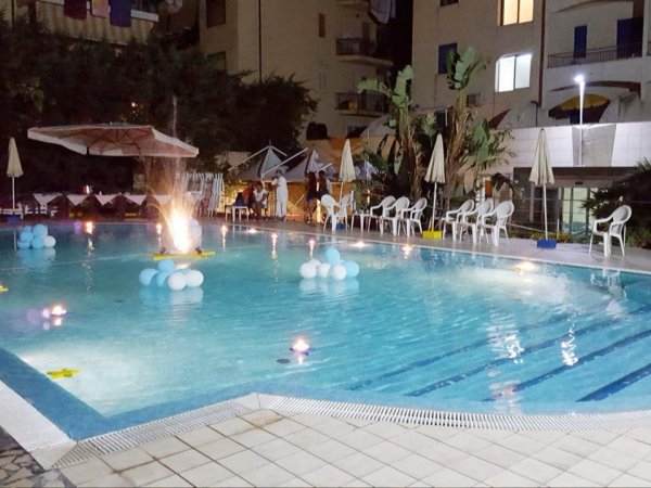 Piscina illuminata di notte con decorazioni galleggianti.