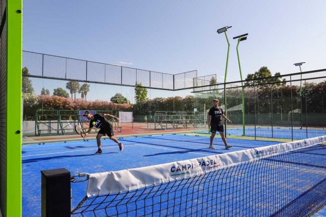 Campo da padel con superficie blu e due persone che giocano.