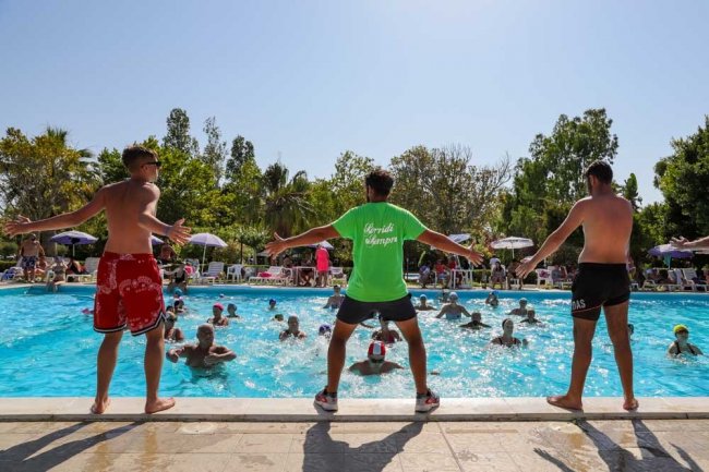Tre persone animano un gruppo in piscina durante una lezione di fitness.
