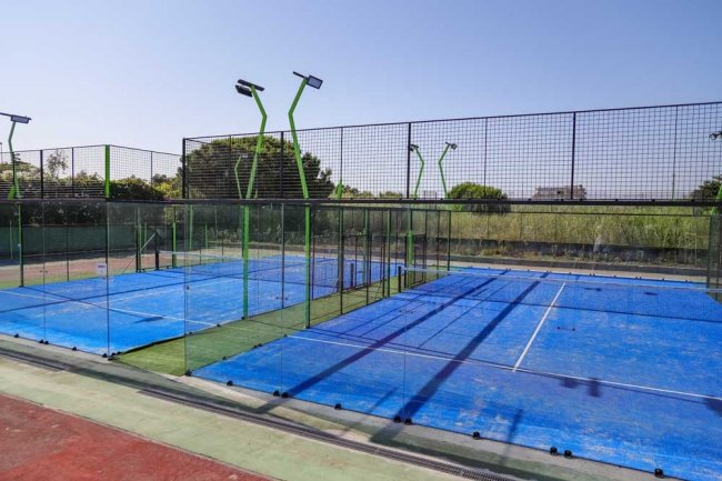 Campi da padel con recinzioni in vetro e pali di illuminazione verde.