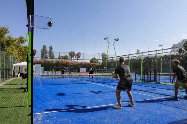 Quattro giocatori su un campo da padel blu, illuminato dal sole.