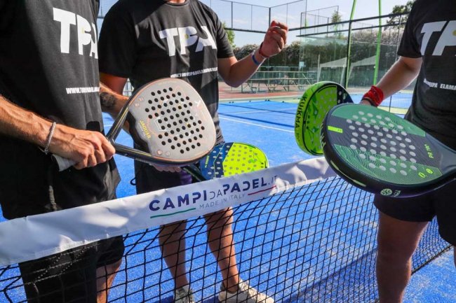 Tre persone con racchette da padel sopra la rete, su campo blu.