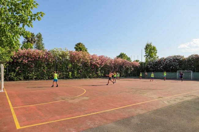 Ragazzi giocano a calcio su un campo all'aperto circondato da alberi fioriti.
