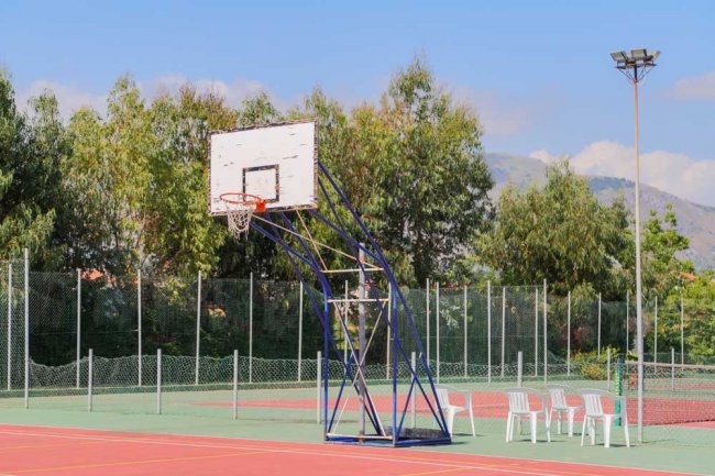 Un campo da basket all'aperto con un canestro e sedie di plastica bianche accanto.
