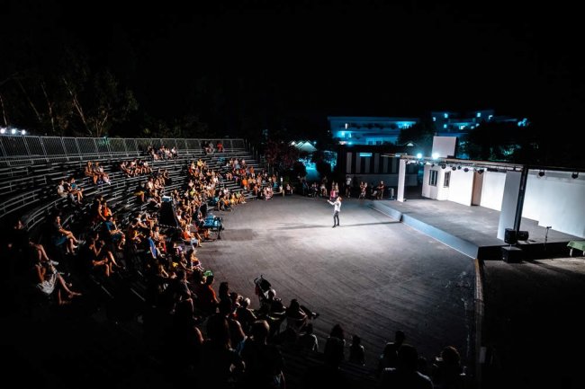 Un anfiteatro pieno di persone che assistono a uno spettacolo notturno.
