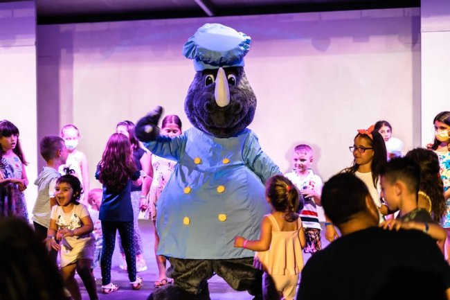 Una mascotte rinoceronte in divisa da chef balla con bambini sul palco.