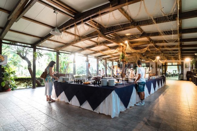 Persone servono cibo da un lungo buffet coperto da tovaglie blu e bianche sotto un tetto aperto.