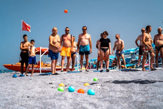 Gruppo di persone in costume da bagno gioca a bocce sulla spiaggia.