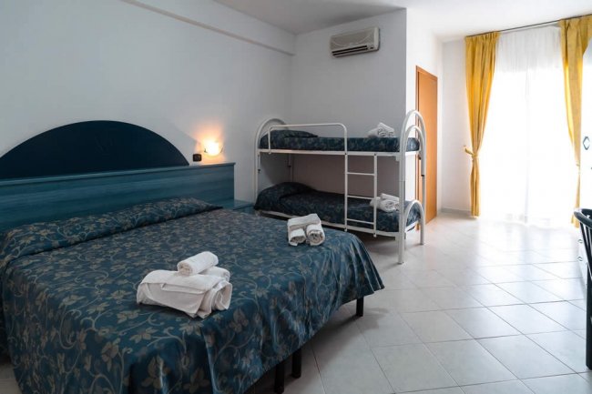 Camera d'albergo con letto matrimoniale, letto a castello e tende gialle.
