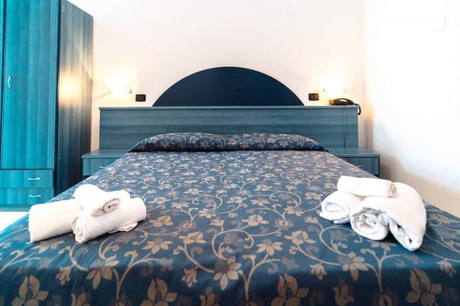 Letto matrimoniale con copriletto blu ornato e asciugamani piegati.