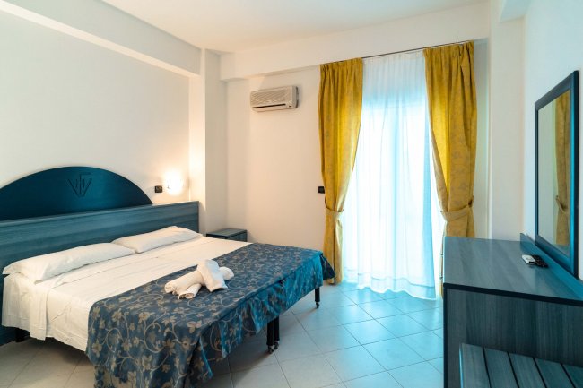 Stanza d'albergo con letto matrimoniale, tenda gialla e arredi blu.