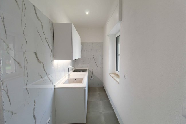 Cucina stretta con mobili bianchi e pareti effetto marmo.