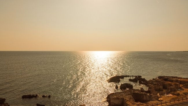 Tramonto su mare e scogli illuminati dal sole.