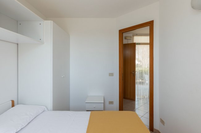 Camera bianca con letto, armadio e porta aperta.