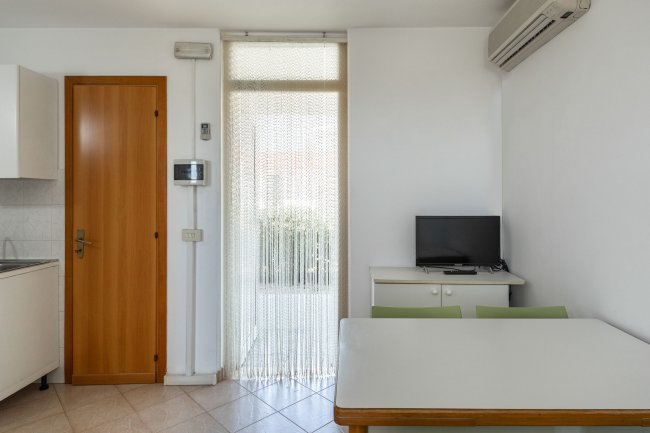 Stanza luminosa con tavolo, sedie e piccolo televisore.