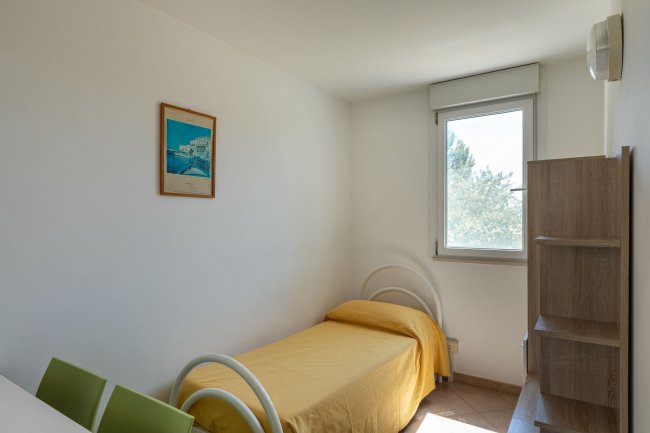 Letto singolo con copriletto giallo sotto una finestra, quadro alla parete.