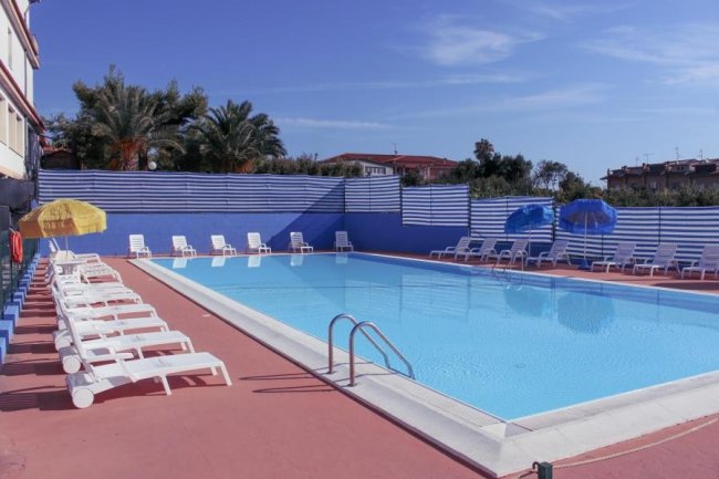 Piscina con lettini, ombrelloni e cielo sereno.