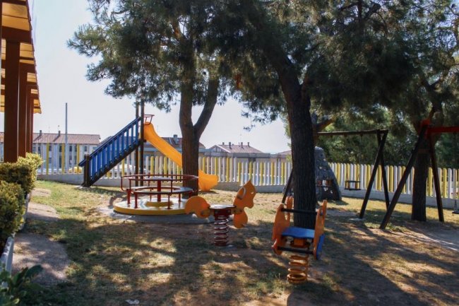 Parco giochi con scivolo e altalene tra alberi.