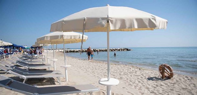 Spiaggia con lettini e ombrelloni bianchi.