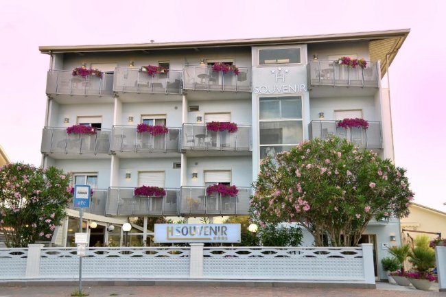Facciata di un albergo con balconi fioriti e cielo rosa.