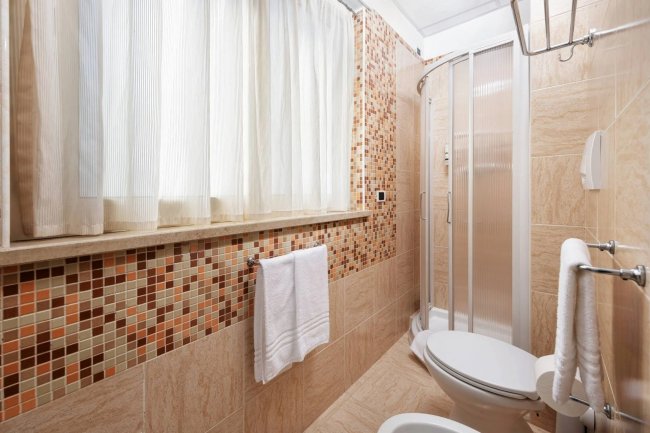 Bagno con doccia angolare e piastrelle a mosaico.