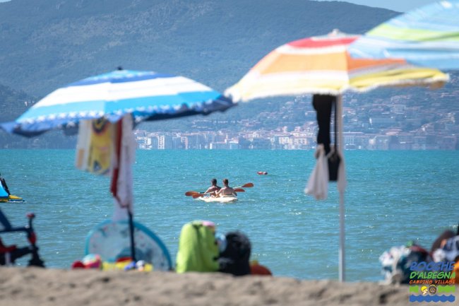 Persone in kayak sul mare, viste da una spiaggia con ombrelloni colorati.