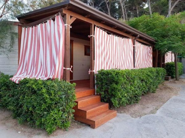 Casetta in legno con tende a strisce, circondata da cespugli.