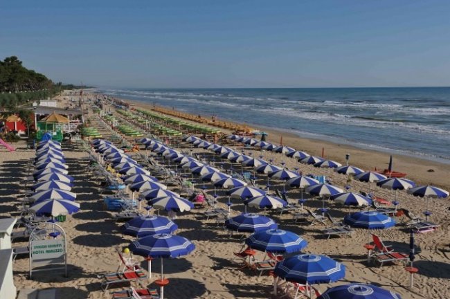 Spiaggia attrezzata con file di ombrelloni blu e bianchi.